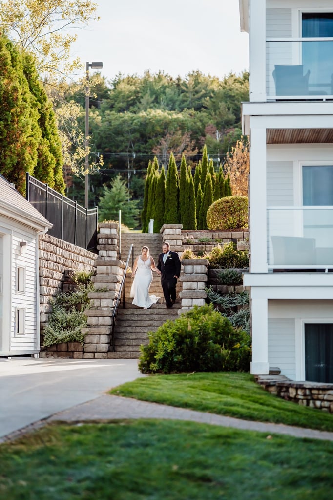 Bride and groom walking hand-in-hand down stone steps surrounded by greenery at a Bar Harbor waterfront venue, heading to their sunset cruise celebration.