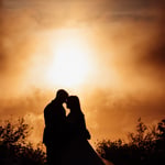 Silhouette of bride and groom at sunset with clouds creating fog