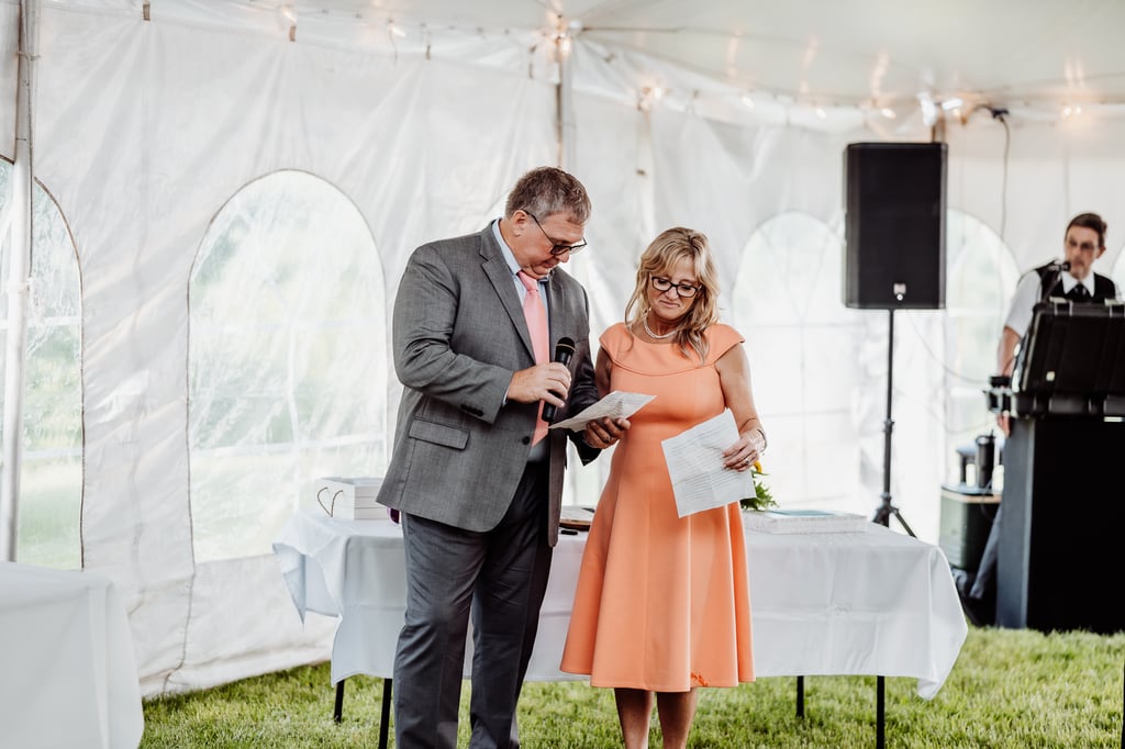 A couple reads from notes at a wedding reception.