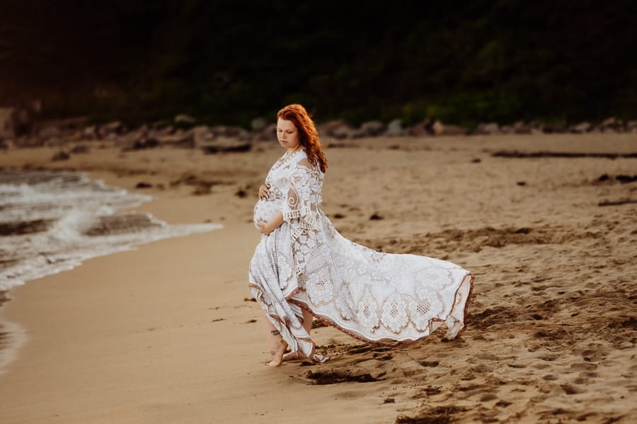 Woman embracing pregnancy on sand beach in acadia