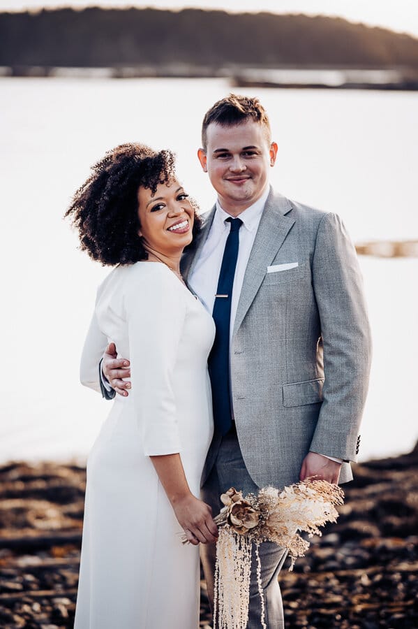 A bride smiling and standing next to groom on a cliff in Maine