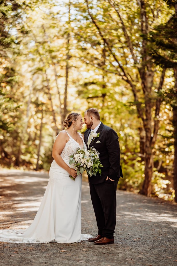 Romantic fall wedding photo of the couple standing close on a wooded path in Acadia National Park.