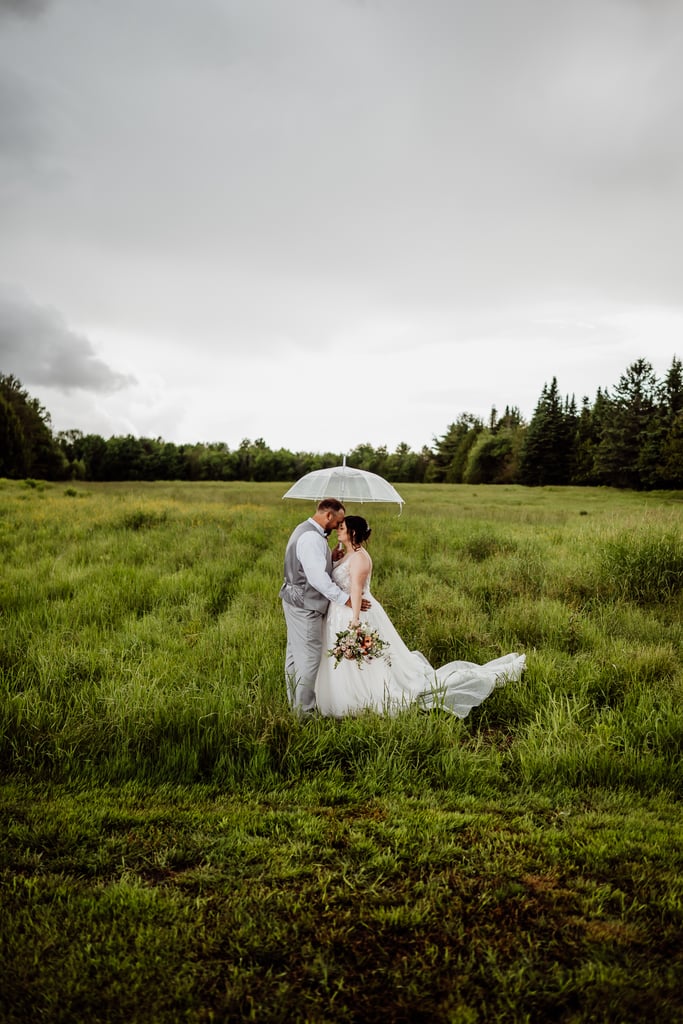 Bride and groom standing in a field with a clear umbrella