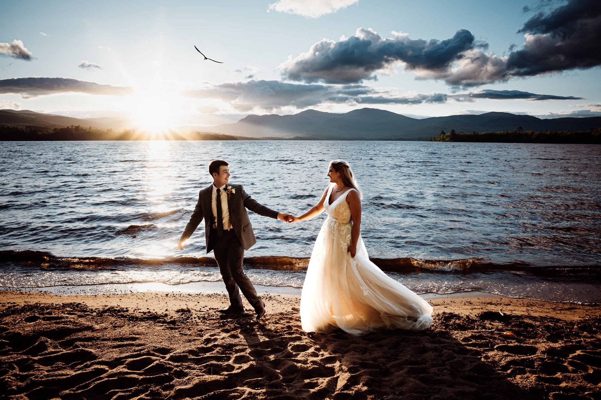 Bride and groom walking together in front of lake at sunset time