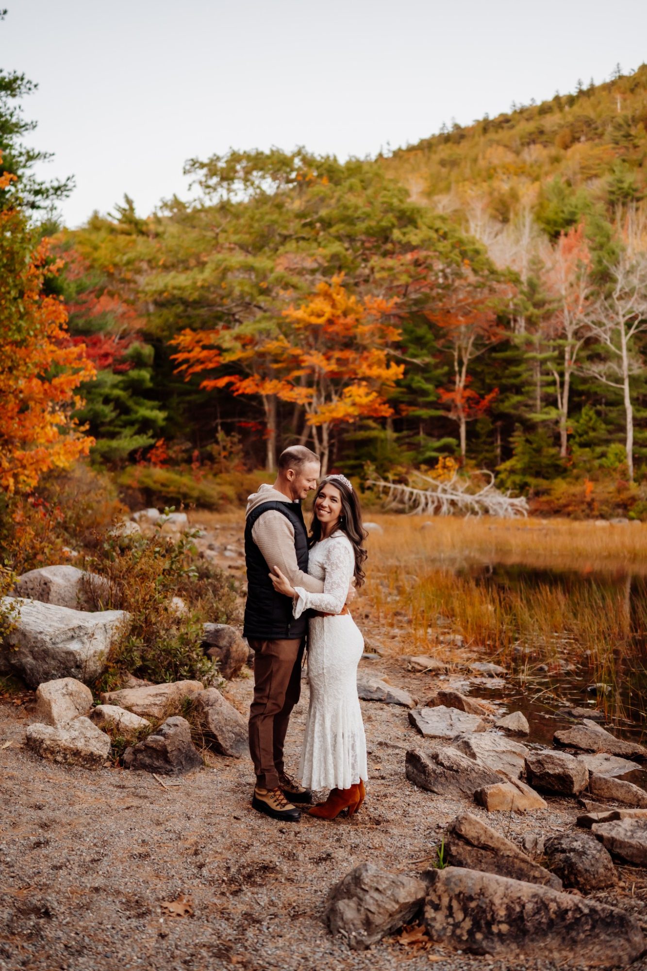 Couple embracing beside golden autumn trees during fall elopement in Acadia National Park.