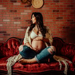 Woman sitting on red antique couch for maternity photos