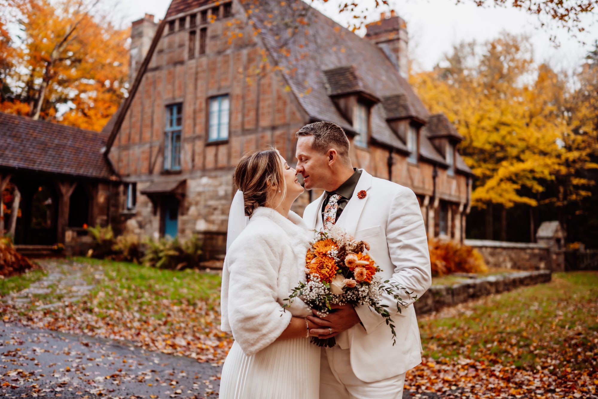 Bride and groom with bouquet outside historic Acadia lodge in autumn.