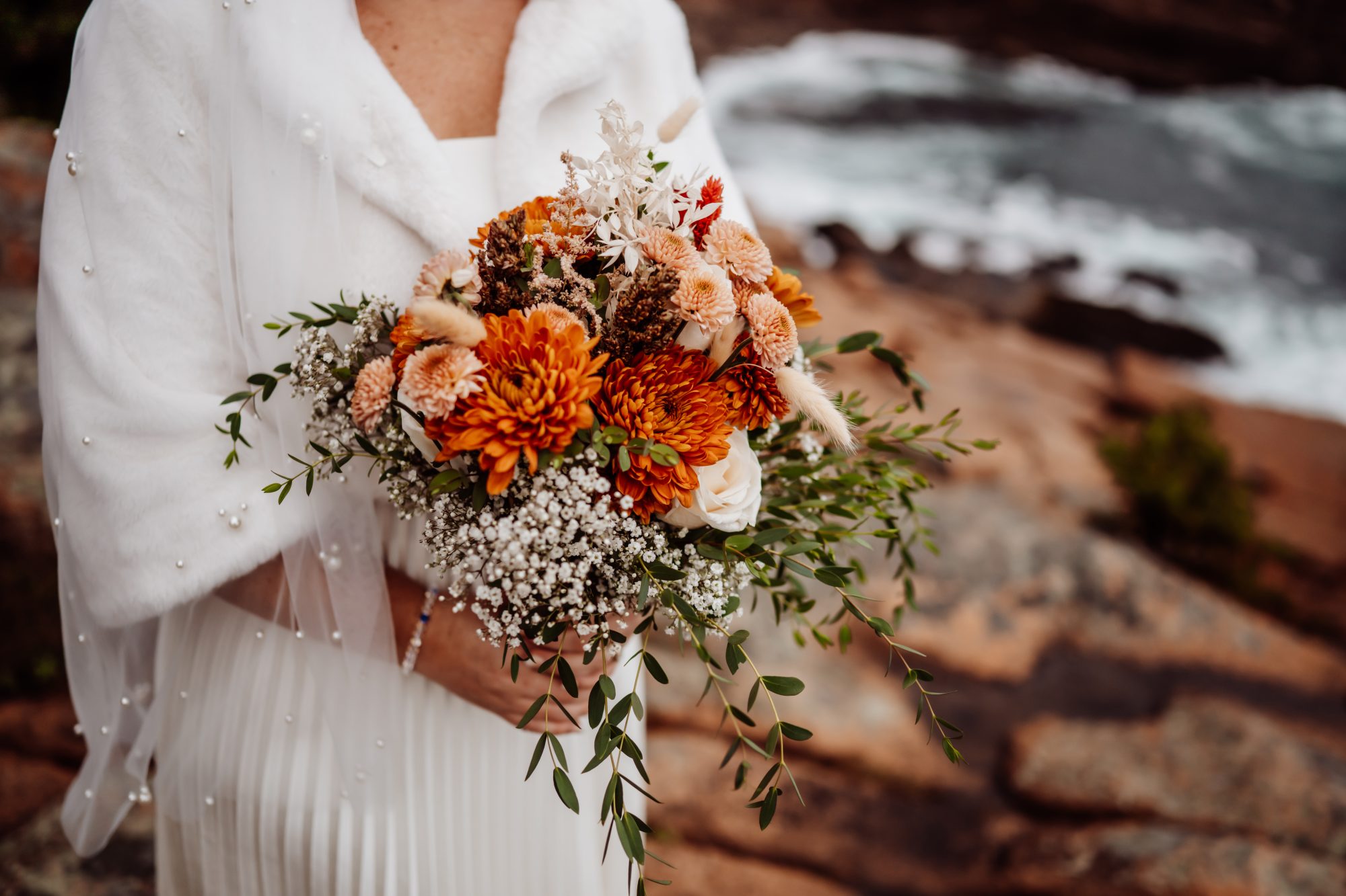 Fall bouquet with orange florals against rocky shoreline at Thunder Hole in Acadia.
