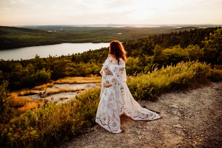 Woman holding pregnant stomach in white lace dress on mountain