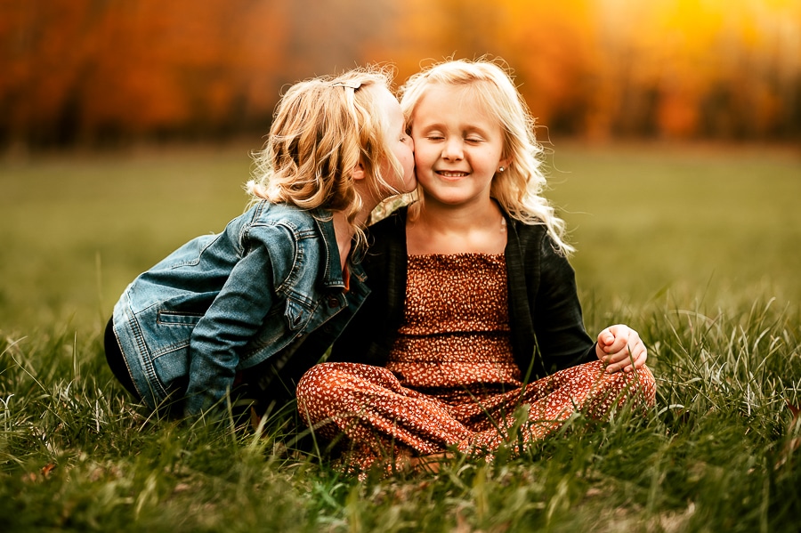 Two blonde children sitting in a field in the fall