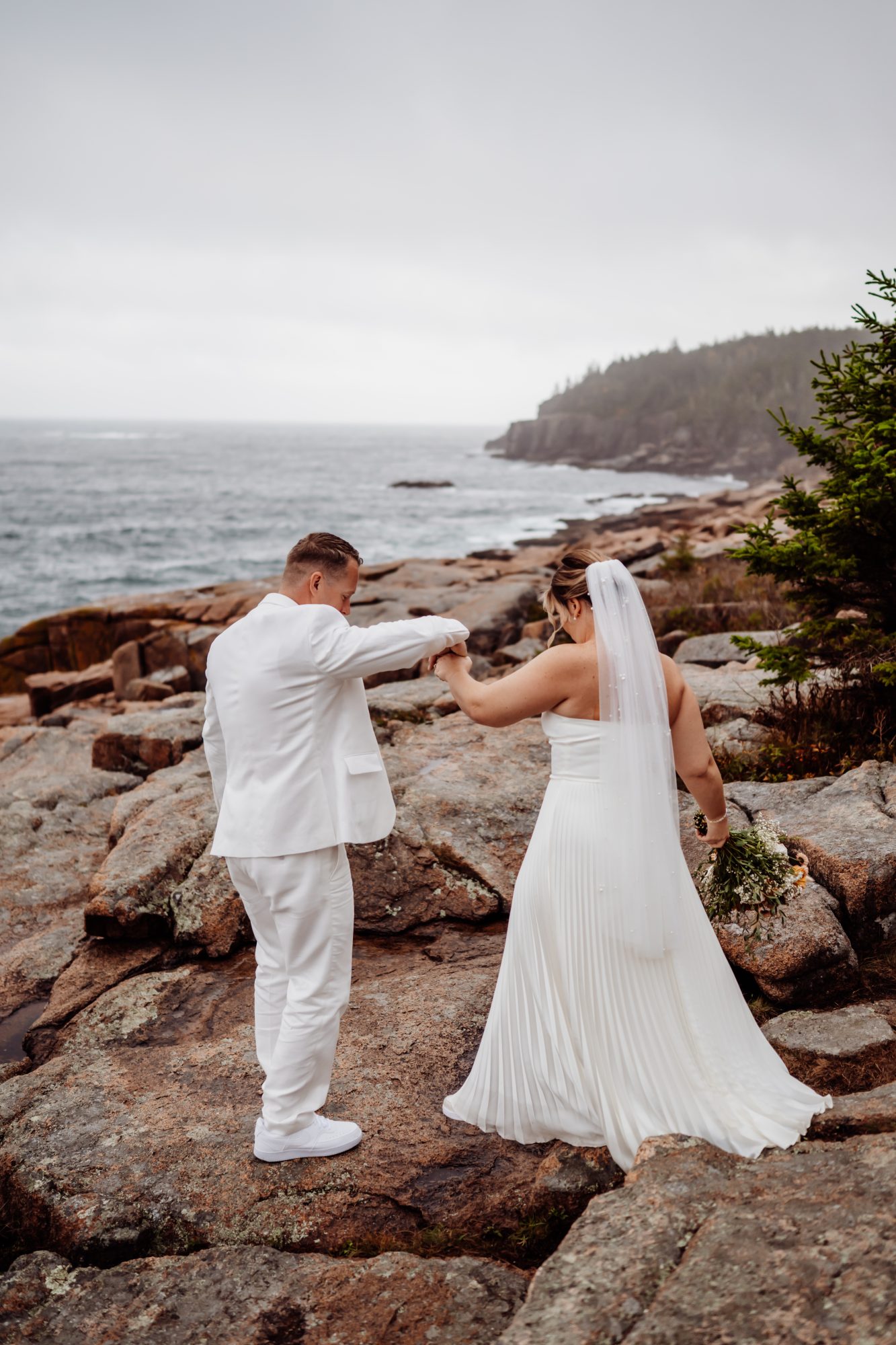 Bride and groom walking hand in hand across granite cliffs during their Thunder Hole elopement in Acadia National Park.