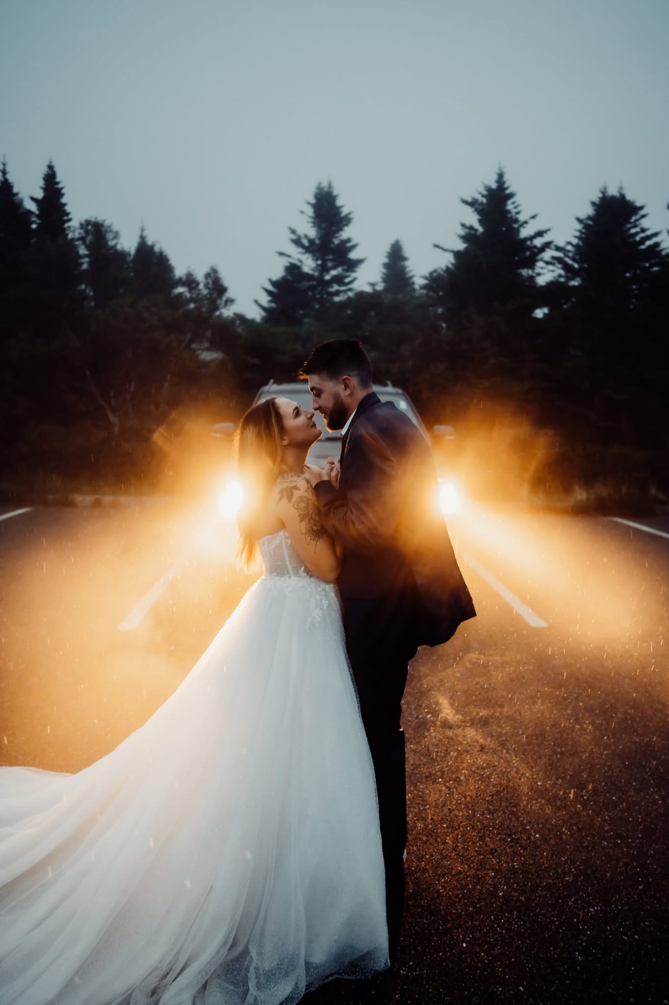 Bride and groom standing together in front of a truck with headlights on in the fog