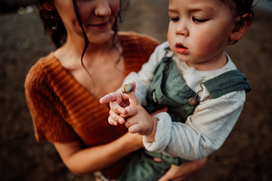 Little boy holding shell on finger wearing green overalls