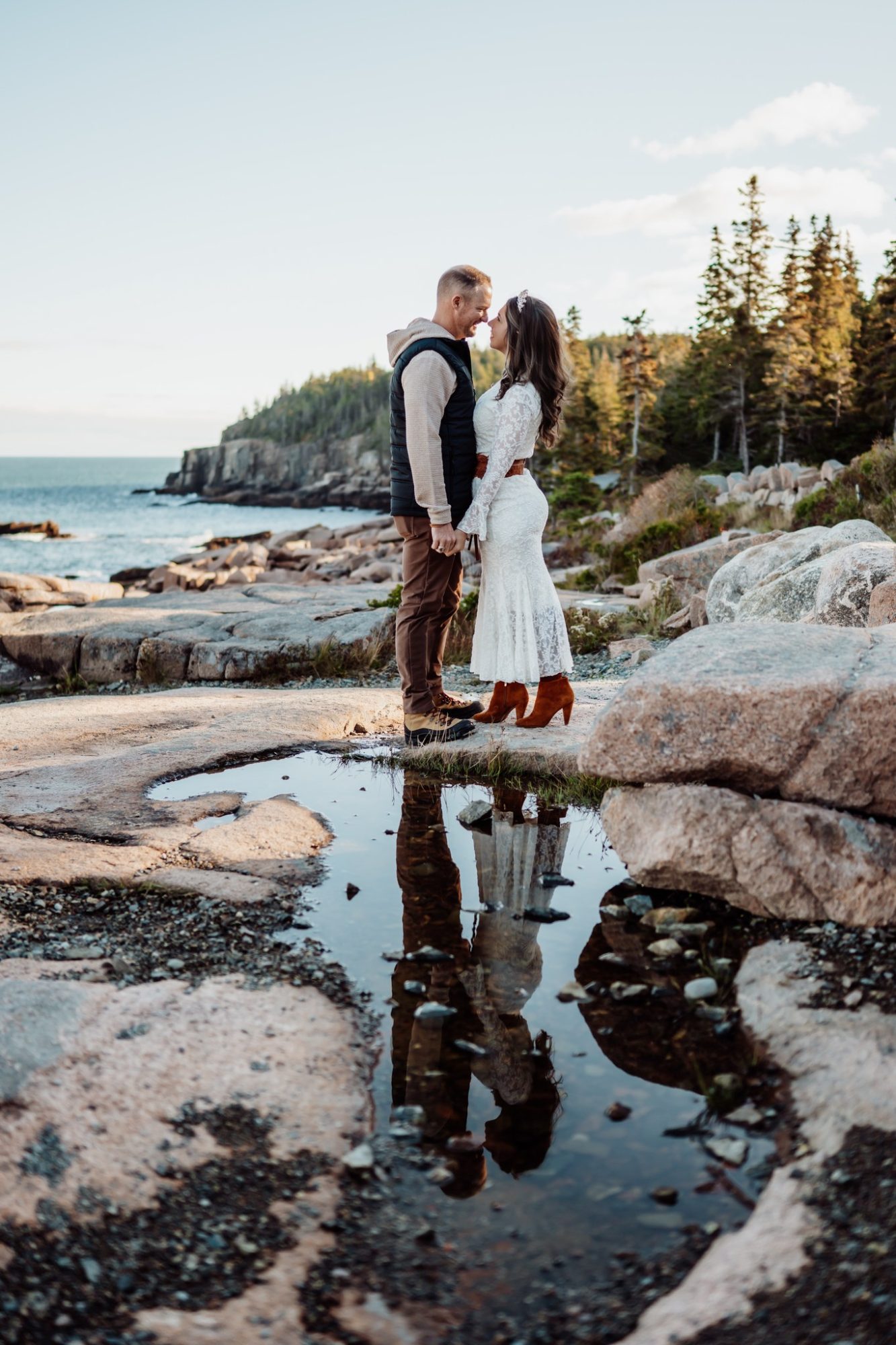 Bride and groom standing on coastal rocks with ocean backdrop in Acadia.
