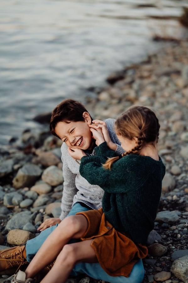 Little girl tickling brother sitting on beach