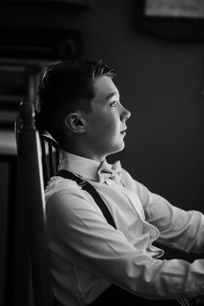 A black and white profile of a young boy in formal attire, sitting and gazing thoughtfully.