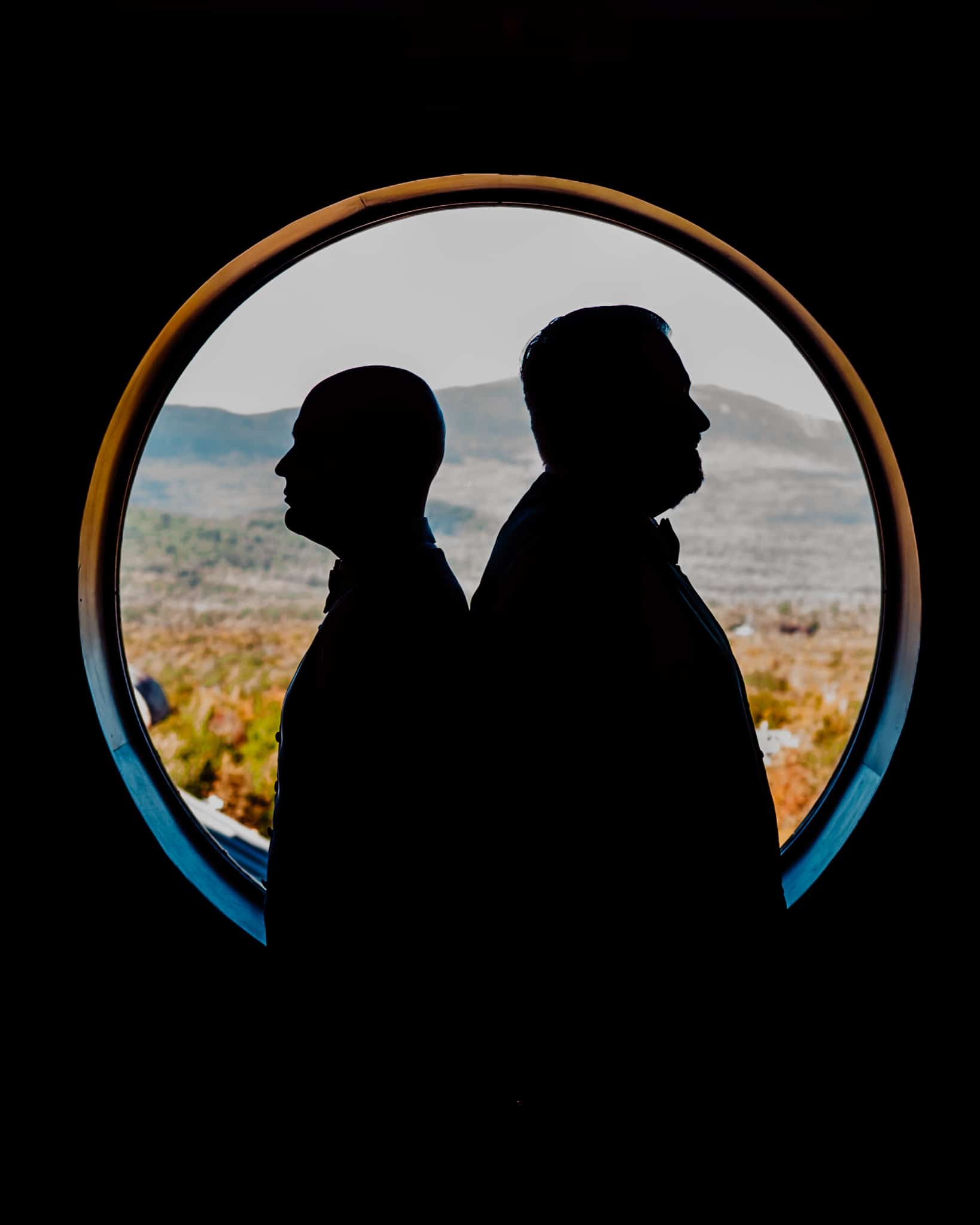 Groom standing back to back being framed by a circle window