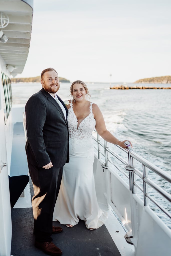 Bride and groom smiling together on a private charter boat in Bar Harbor, Maine, with ocean waves and islands behind them.