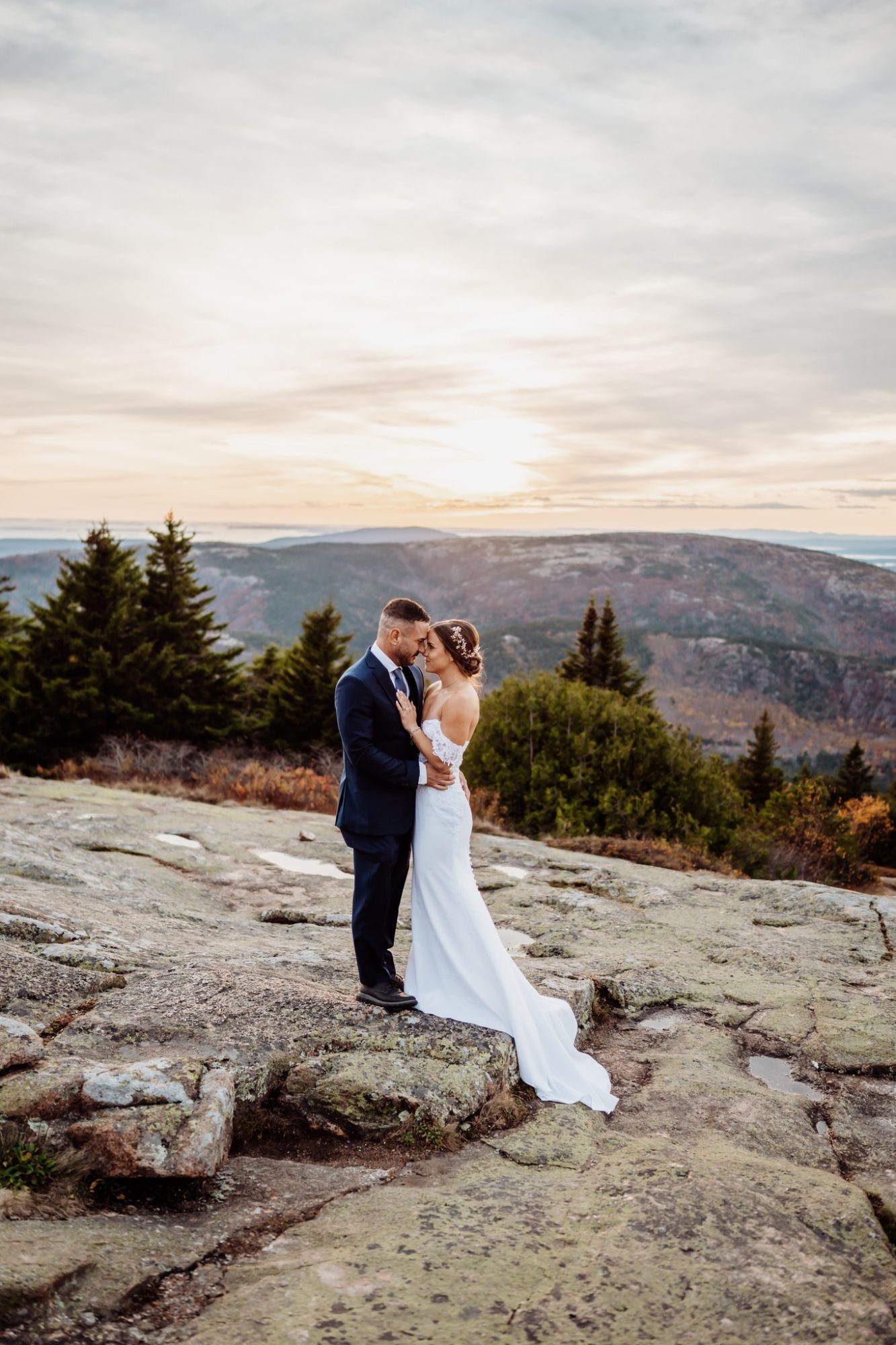 Wide landscape portrait of bride and groom at Schooner Head Overlook in Acadia National Park at golden hour.