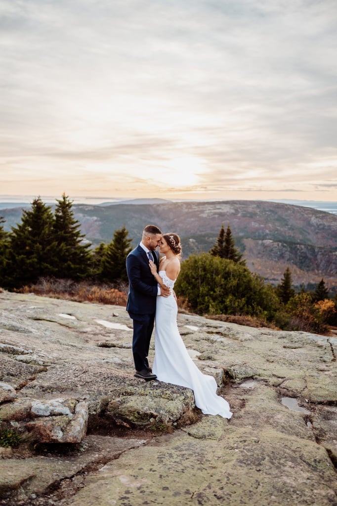 Wide landscape portrait of bride and groom at Schooner Head Overlook in Acadia National Park at golden hour.