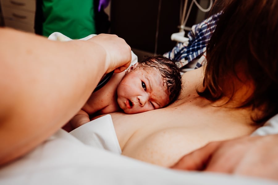 Newborn baby laying on mothers chest looking