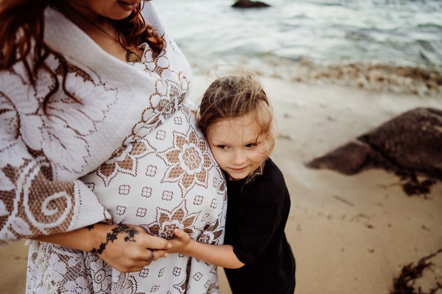 little boy hugging mothers belly on beach