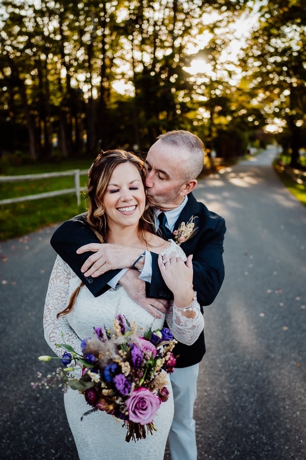 Groom with arms wrapped around broad shoulders kissing her cheek