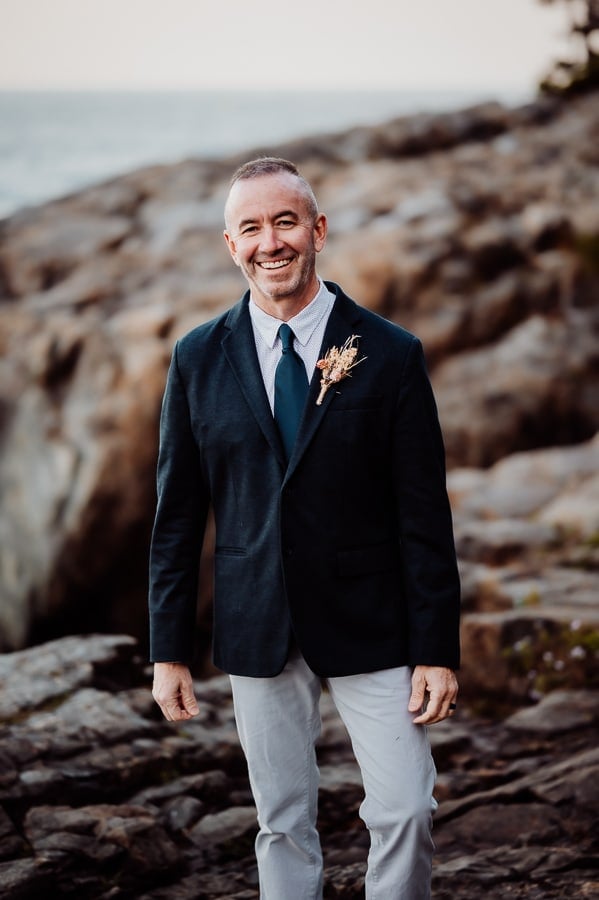 Groom smiling in front of ocean cliffs in Acadia national park