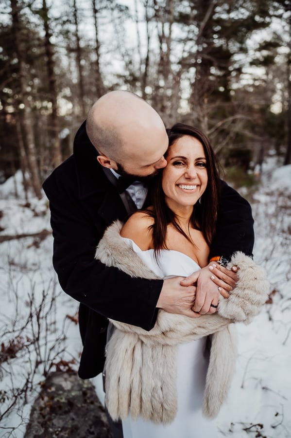 Bride wrapped in grooms arms outside in the winter snow