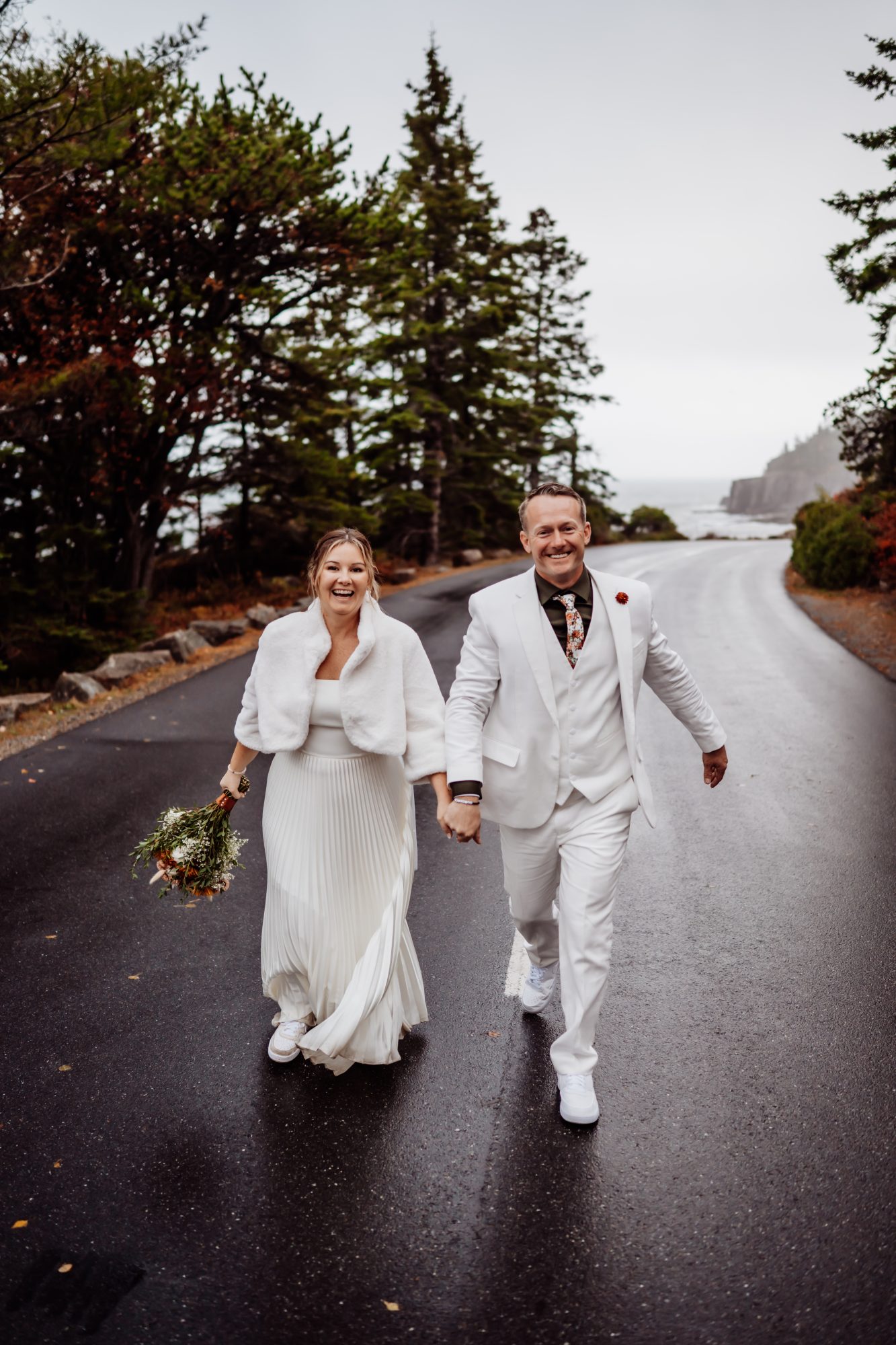 Couple running together along Park Loop Road in Acadia National Park after elopement.