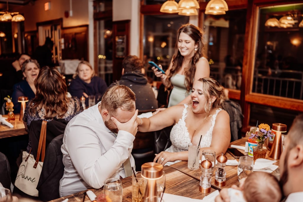 Bride and groom burst into laughter during a funny wedding toast surrounded by close friends and family at their Bar Harbor dinner reception.