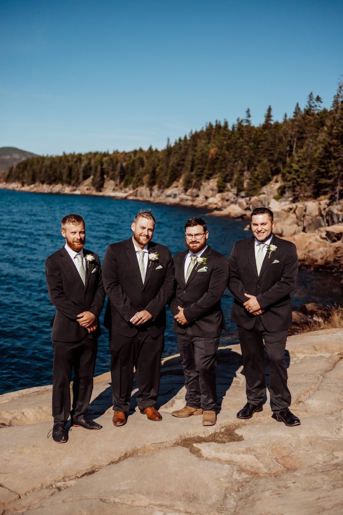 Groom standing with his groomsmen in black suits and light green ties, overlooking the ocean cliffs at Otter Point in Acadia National Park near Bar Harbor, Maine.