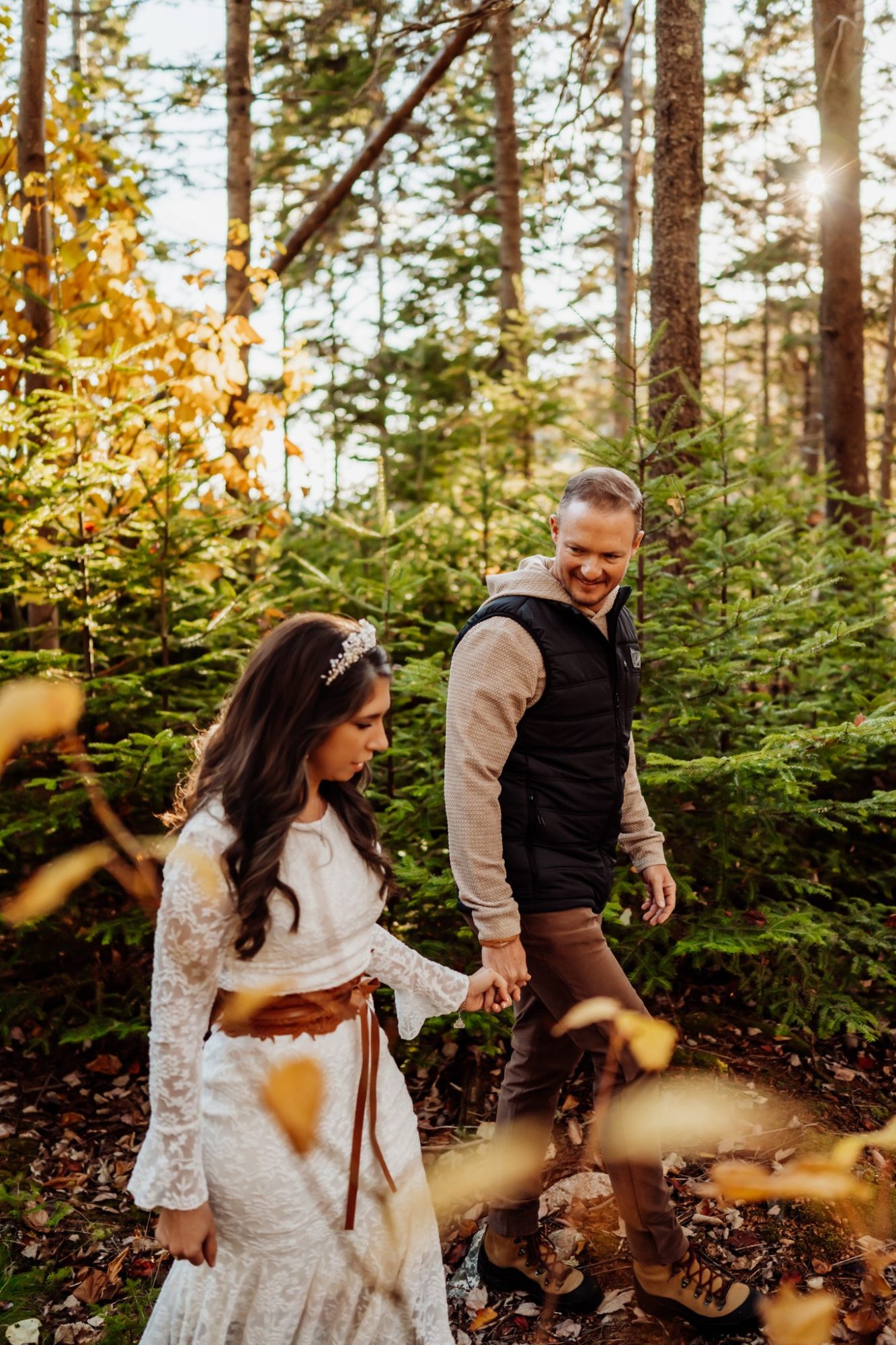 Couple strolling through sunlit forest during autumn elopement in Acadia National Park.