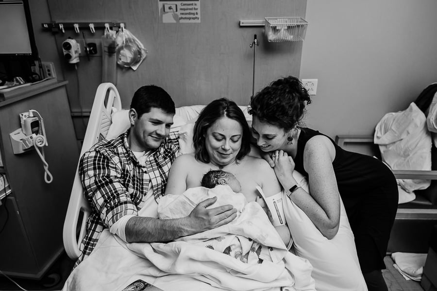 Family sitting in a hospital bed looking at brand new baby after