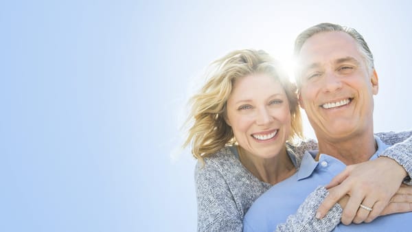 A smiling middle-aged couple outdoors against a bright blue sky