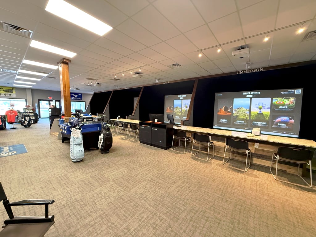 The simulator bays at Tilbury Golf Academy: a row of TrackMan screens with counter seating beside the pro shop