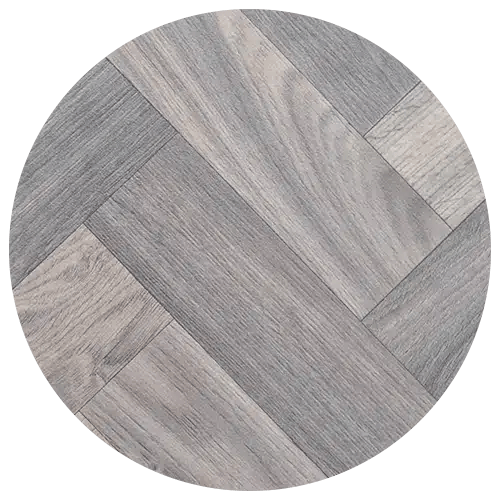 A round sample of gray wooden floor tiles arranged in a herringbone pattern, featuring various light and dark gray wood grain textures—perfect for adding style to your kitchen remodel.