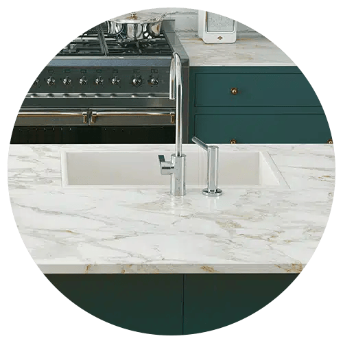 A modern kitchen remodel featuring a marble countertop, built-in sink with a chrome faucet, green cabinetry, and a stainless steel stove in the background.