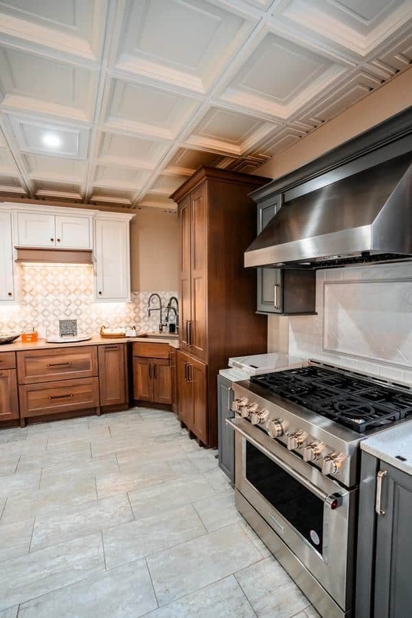 Modern kitchen with stainless steel gas stove and range hood, brown and white cabinetry, geometric tiled backsplash, and light tile flooring—an inspiring design featured in our Spencerport Showroom.