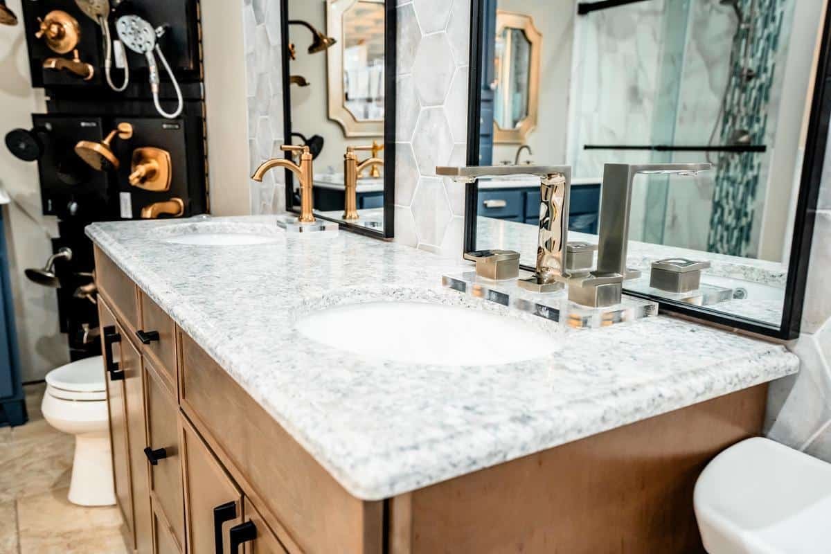 Modern bathroom with a white marble double sink vanity, gold and silver faucets, wooden cabinets, and large mirrors—discover these stylish bathroom fixtures on display at the Spencerport Showroom.