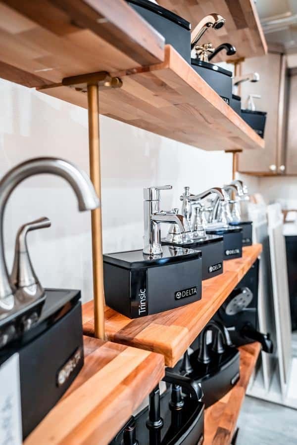A display of various modern kitchen and bathroom faucets mounted on wooden shelves in the Spencerport Showroom, showcasing different designs and finishes.