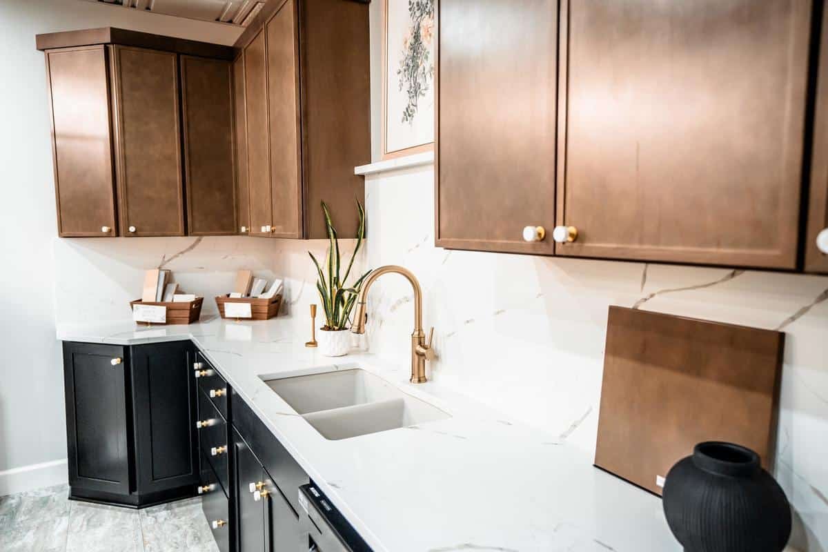 Modern kitchen with brown upper cabinets, black lower cabinets, white marble countertops and backsplash, a brass faucet, a double sink, and stylish decor—perfect inspiration for your Spencerport home or next showroom visit.