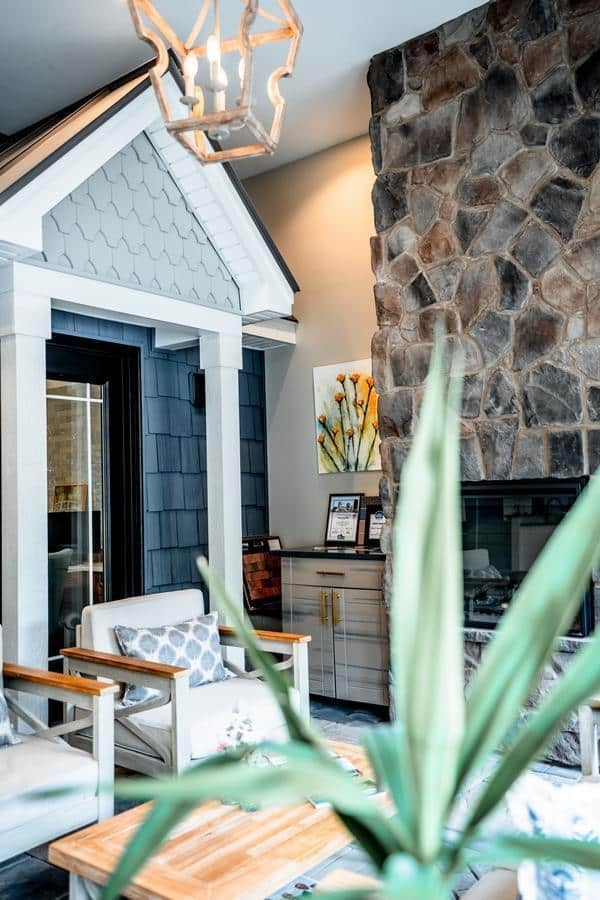 A cozy living room with armchairs, a wooden coffee table, and a stone fireplace features house-like decor and wall art—much like the inviting setups at the Spencerport Showroom. Warm lighting and homey details create a welcoming atmosphere.