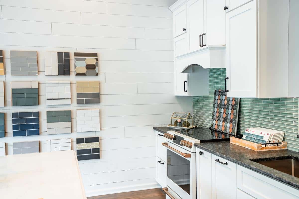 Modern kitchen with white cabinets, black countertops, green tile backsplash, and a display wall featuring various tile samples—just one of the highlights at the Spencerport Showroom.