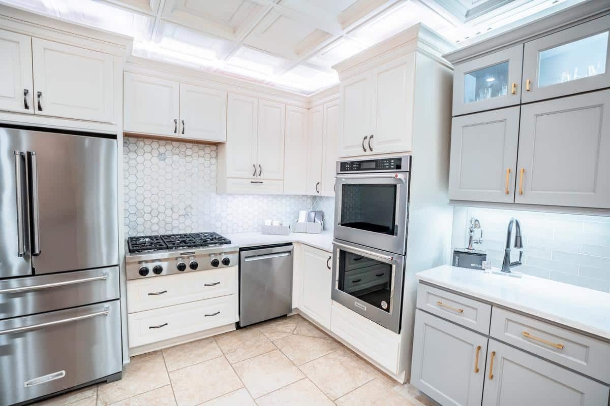 Modern Spencerport kitchen with white cabinets, stainless steel appliances, hexagonal tile backsplash, and under-cabinet lighting—showroom-level design on clean countertops.