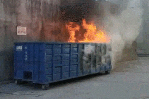 A dumpster is engulfed in flames. Fire and smoke are visible.