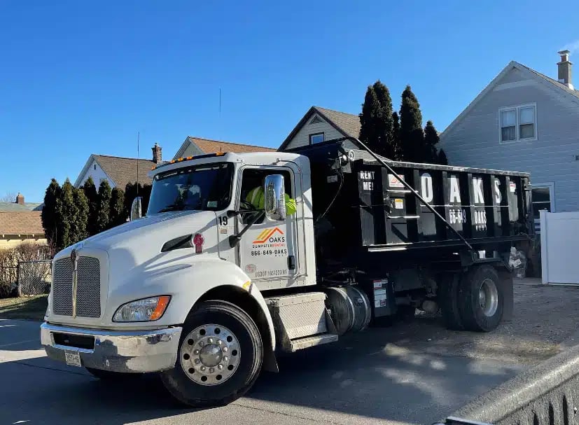 A white dump truck with a black bed parked on a street. The truck has a logo on the side.