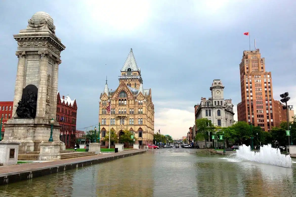 a large building with a clock tower and a fountain in front of it, with a statue on the left side of the image