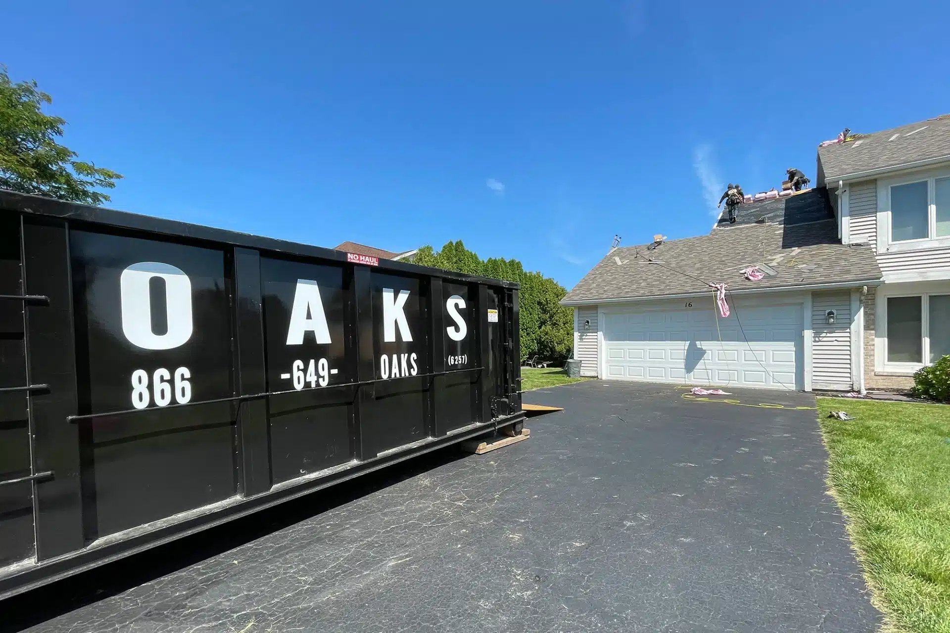 A large black dumpster with Oaks logo on residential property. Oaks provides waste removal services.