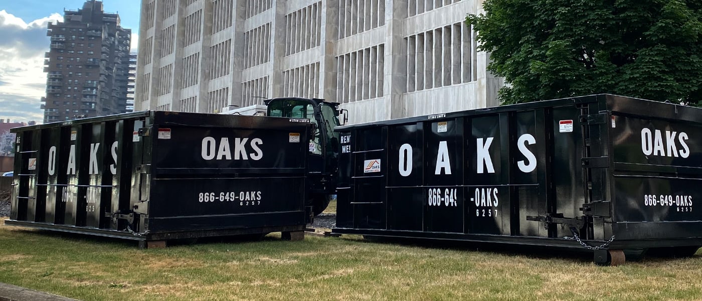 Two black dumpsters with Oaks logo on side